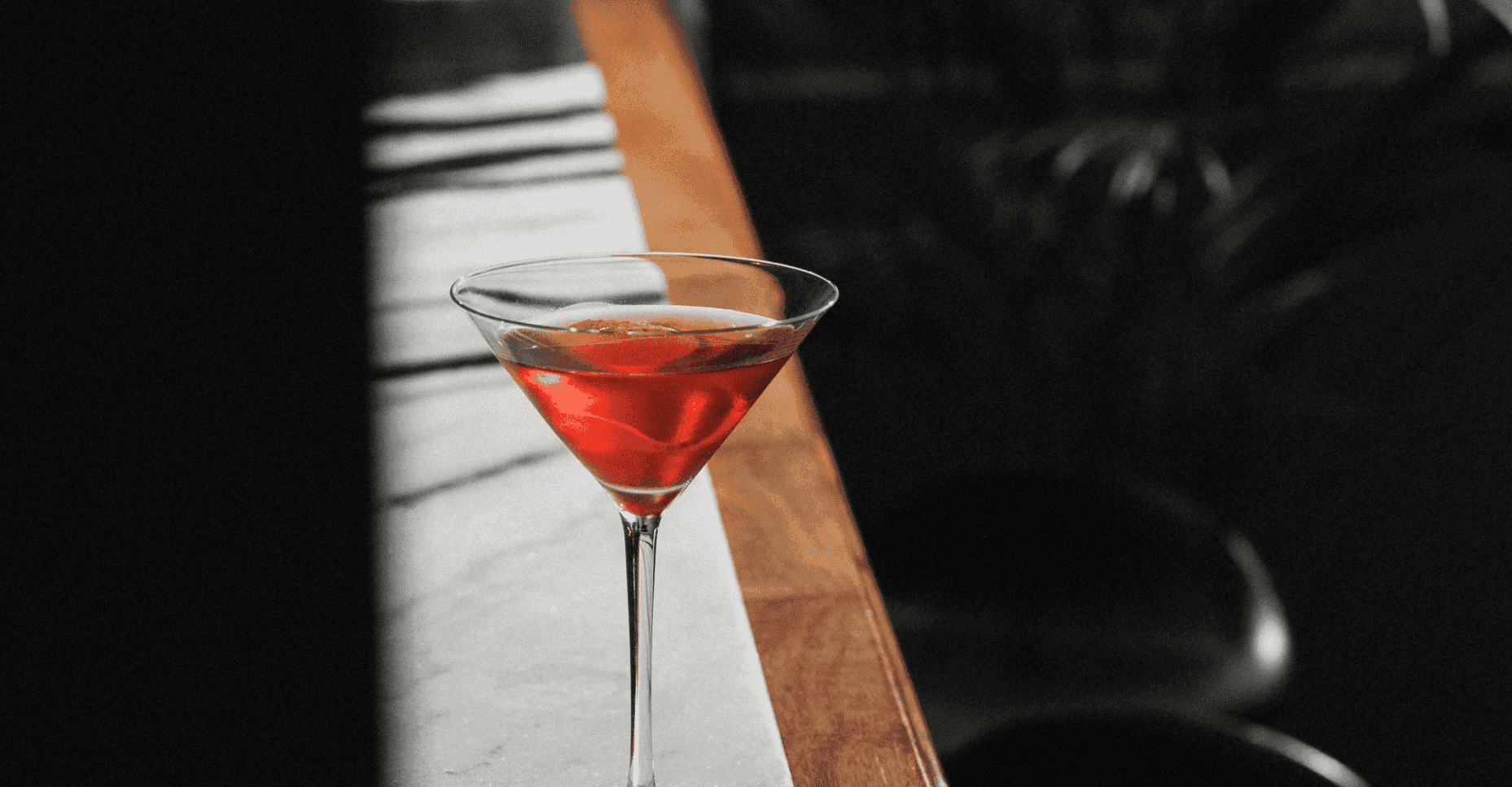 A martini glass filled with a red cocktail sits on a bar counter.